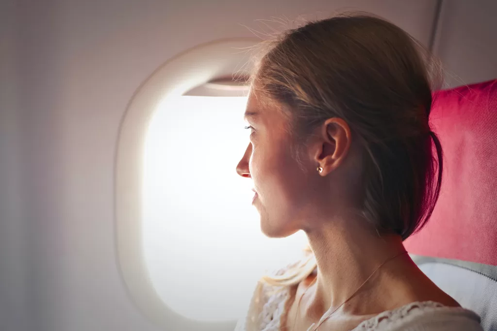 A woman with fair hair is on a plane and looking out a window