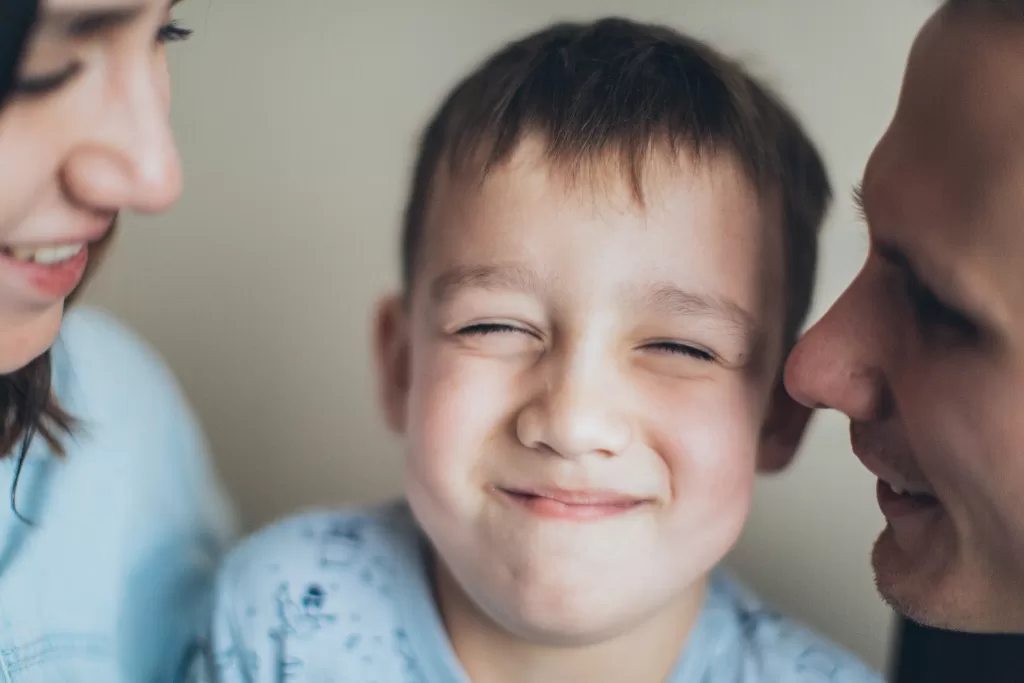 Two parents and a young boy smiling in the middle with his eyes closed. They are all smiling