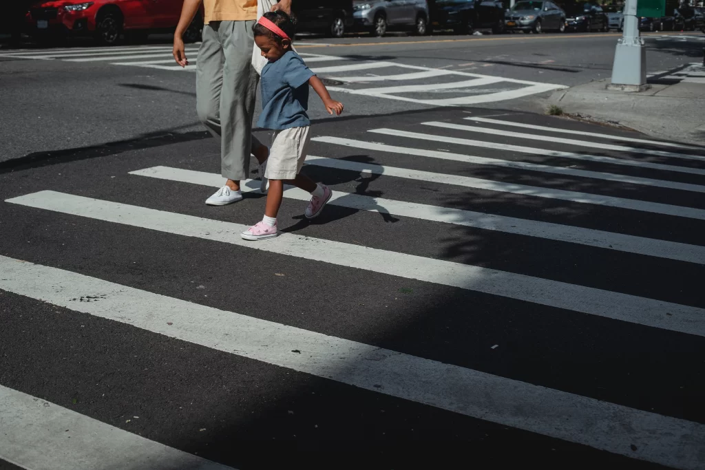 A child holds their mother's hand as they cross a black and white crossing