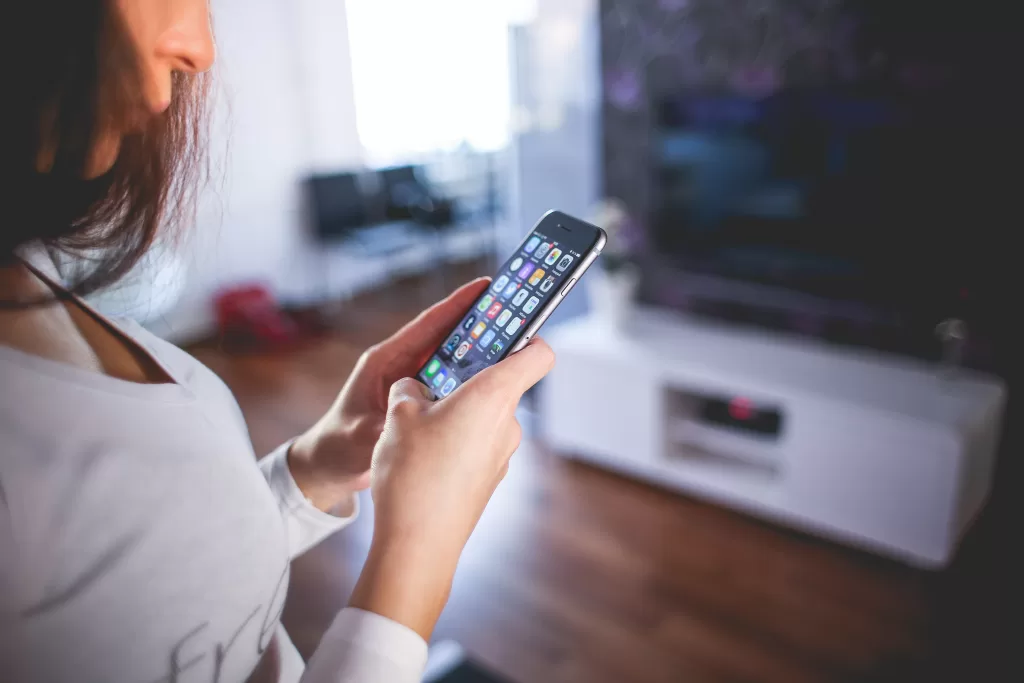 A woman staring down at her phone. She is in an apartment with wooden floors and a TV is in view