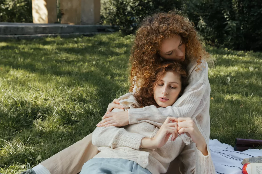 Two women in an embrace on a picnic blanket on the ground. 