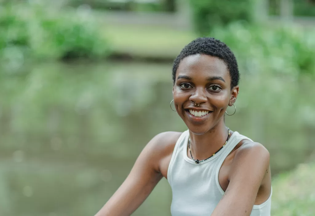 A brown woman with short hair is wearing a white tank top and smiling at the camera